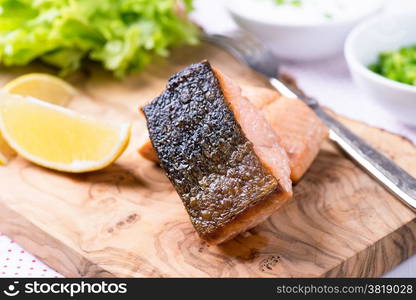 Grilled red fish fillet with lemon and green salad on wooden beard, selective focus