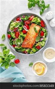 Grilled salmon fish fillet and fresh green leafy vegetable salad with tomatoes, red onion and broccoli. Healthy food. Ketogenic lunch. Top view
