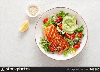 Grilled salmon fish fillet and fresh green lettuce vegetable tomato salad with avocado guacamole, top view.