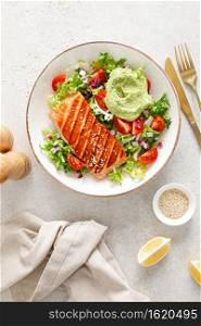 Grilled salmon fish fillet and fresh green lettuce vegetable tomato salad with avocado guacamole. Top view