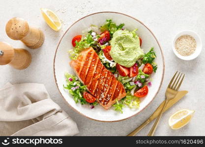 Grilled salmon fish fillet and fresh green lettuce vegetable tomato salad with avocado guacamole. Top view