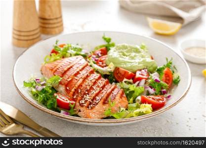 Grilled salmon fish fillet and fresh green lettuce vegetable tomato salad with avocado guacamole