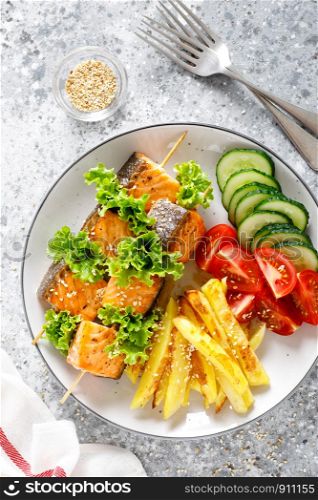 Grilled salmon kebab on skewers with baked potato, fresh cucumbers and tomatoes