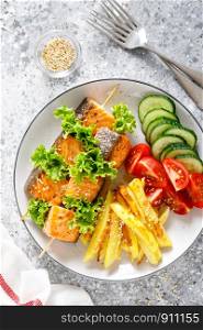 Grilled salmon kebab on skewers with baked potato, fresh cucumbers and tomatoes