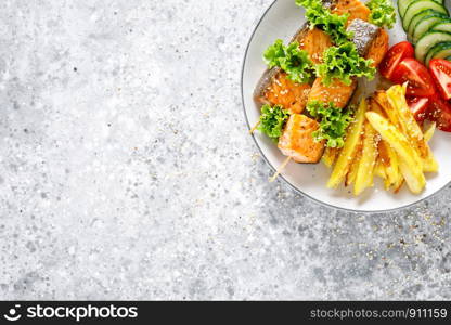 Grilled salmon kebab on skewers with baked potato, fresh cucumbers and tomatoes