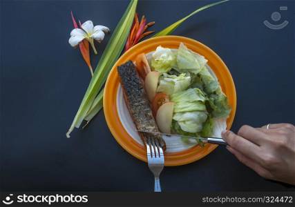 Grilled salmon steak served with vegetable salad on a black table