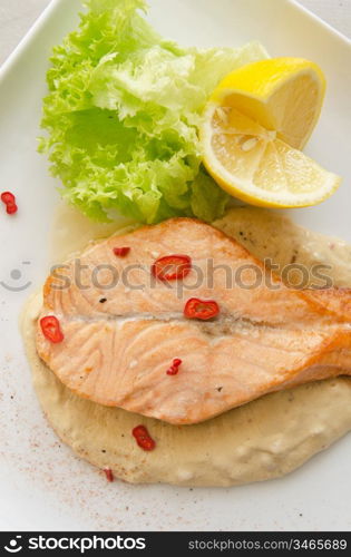 Grilled salmon steak with greens, lemon, sauce and pepper chile