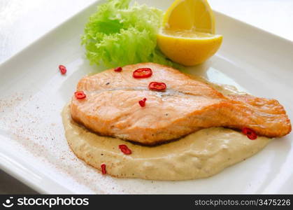 Grilled salmon steak with greens, lemon, sauce and pepper chile