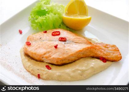 Grilled salmon steak with greens, lemon, sauce and pepper chile