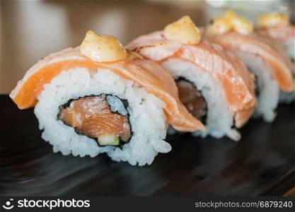 Grilled salmon sushi roll, japanese food style on black ceramic dish