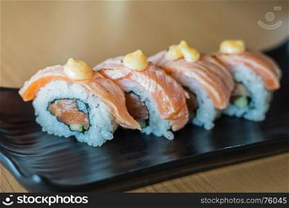 Grilled salmon sushi roll, japanese food style on black ceramic dish.