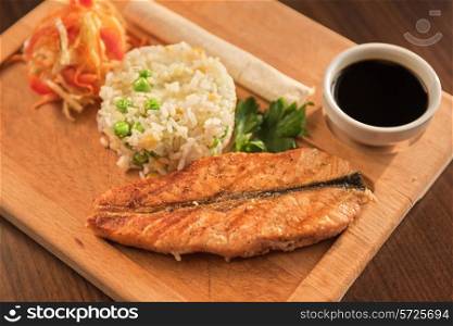 Grilled salmon with rice and vegetables at wooden table