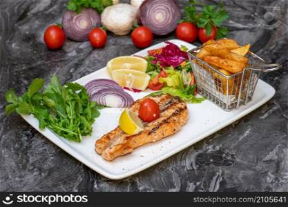 Grilled salmon with salad and french fries on a white plate