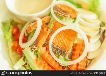 Grilled salmon with salad, onion slice rings, carrot, boiled egg and salad dressing served on white plate. Homemade and healthy food. Selective focus.