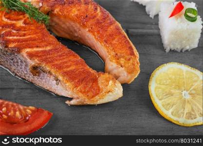 Grilled salmon with vegetables and rice on wooden background