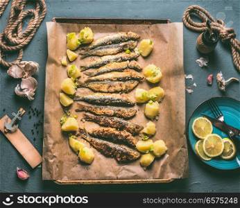Grilled sardines with potatoes on baking tray with ingredients: lemon, garlic and herbs for tasty seafood eating. Cooking preparation of fishes