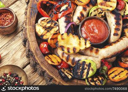 Grilled sausages and vegetables with sauce ketchup on a wooden table.Autumn food. Grilled sausages with vegetables