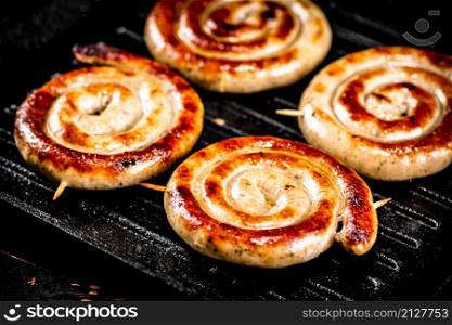 Grilled sausages in a frying pan. On a black background. High quality photo. Grilled sausages in a frying pan.