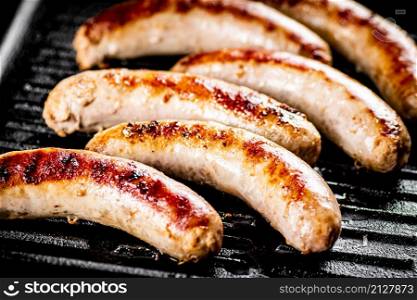Grilled sausages in a frying pan. On a black background. High quality photo. Grilled sausages in a frying pan.