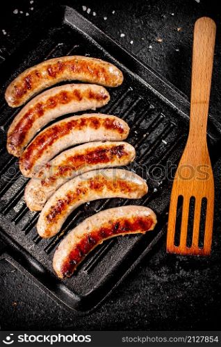 Grilled sausages in a frying pan with a wooden spatula. On a black background. High quality photo. Grilled sausages in a frying pan with a wooden spatula.