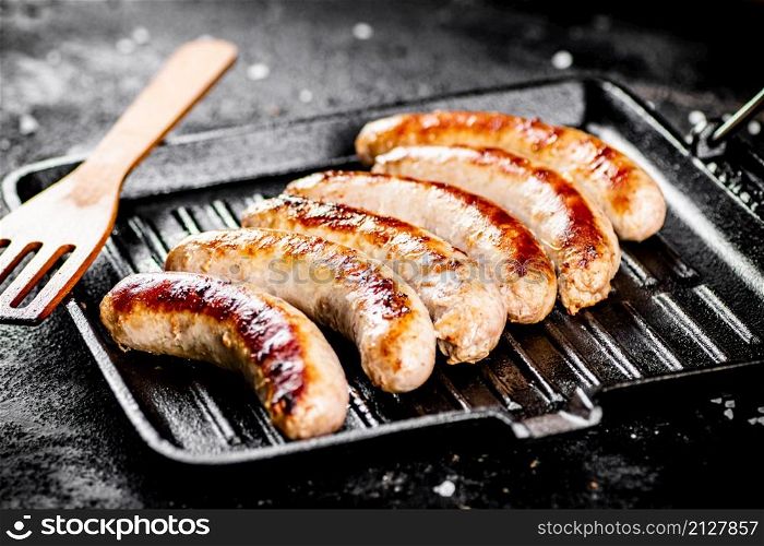 Grilled sausages in a frying pan with a wooden spatula. On a black background. High quality photo. Grilled sausages in a frying pan with a wooden spatula.