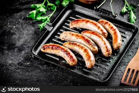 Grilled sausages in a frying pan with parsley. On a black background. High quality photo. Grilled sausages in a frying pan with parsley.