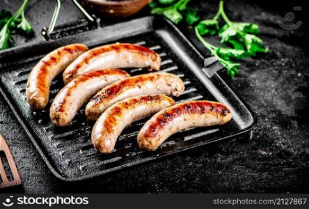 Grilled sausages in a frying pan with parsley. On a black background. High quality photo. Grilled sausages in a frying pan with parsley.