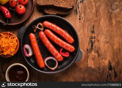 Grilled sausages in a pan with onions and vegetables.