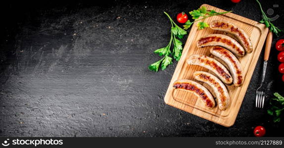 Grilled sausages on a cutting board with tomatoes. On a black background. High quality photo. Grilled sausages on a cutting board with tomatoes.