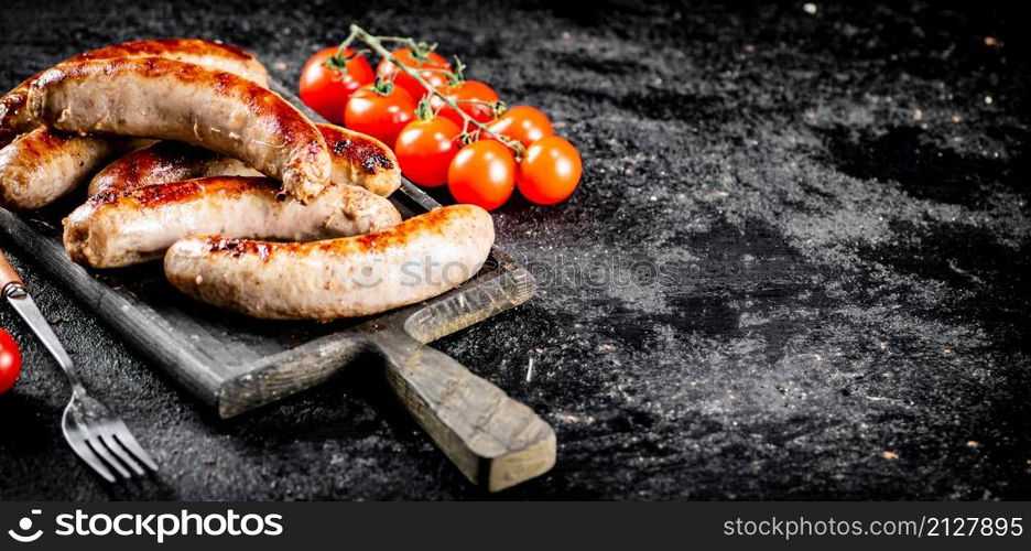 Grilled sausages on a cutting board with tomatoes. On a black background. High quality photo. Grilled sausages on a cutting board with tomatoes.