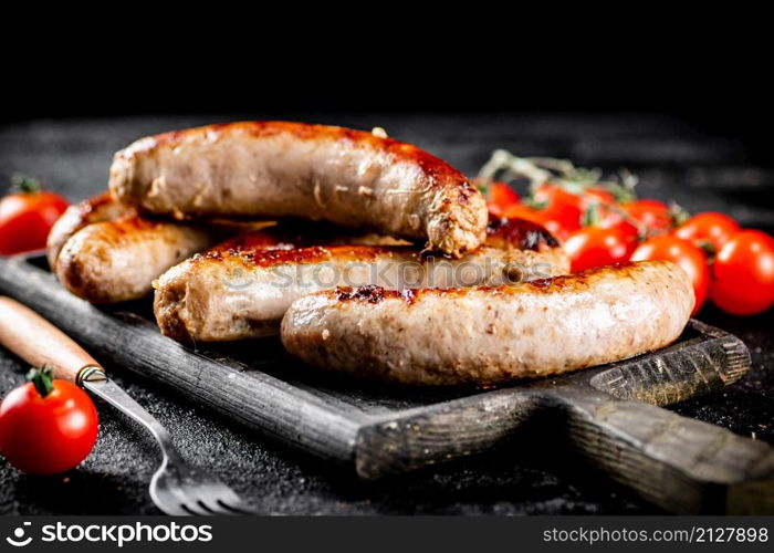 Grilled sausages on a cutting board with tomatoes. On a black background. High quality photo. Grilled sausages on a cutting board with tomatoes.
