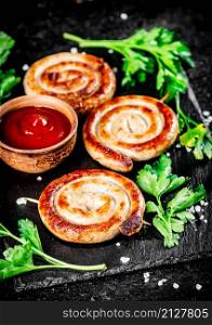 Grilled sausages on a stone board with tomato sauce and parsley. On a black background. High quality photo. Grilled sausages on a stone board with tomato sauce and parsley.
