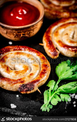 Grilled sausages on a stone board with tomato sauce and parsley. On a black background. High quality photo. Grilled sausages on a stone board with tomato sauce and parsley.