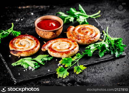 Grilled sausages on a stone board with tomato sauce and parsley. On a black background. High quality photo. Grilled sausages on a stone board with tomato sauce and parsley.