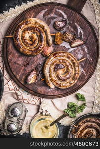 Grilled sausages spiral served on rustic round cutting board with mustard , top view, Country dark style