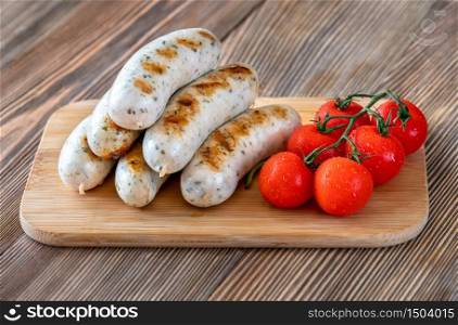 Grilled sausages with bunch of cherry tomatoes on wooden board