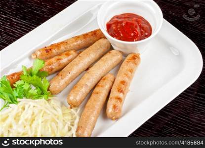 Grilled sausages with cabbage, greens and tomato sauce on white plate