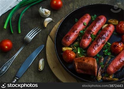 grilled sausages with vegetables and herbs in a frying pan