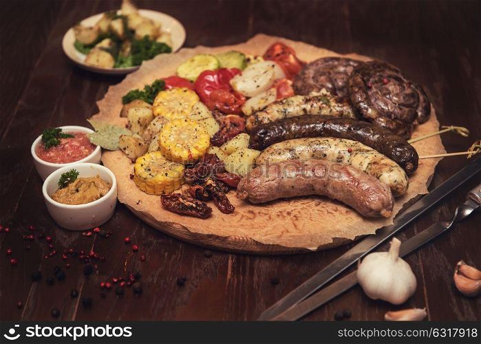Grilled sausages with vegetables. Grilled different meat and fish sausages with vegetables and spices on wooden background