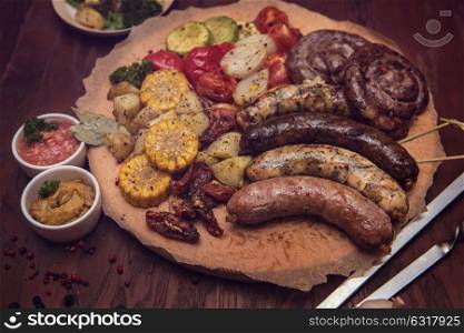 Grilled sausages with vegetables. Grilled different meat and fish sausages with vegetables and spices on wooden background