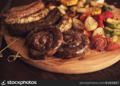 Grilled sausages with vegetables. Grilled different meat and fish sausages with vegetables and spices on wooden background