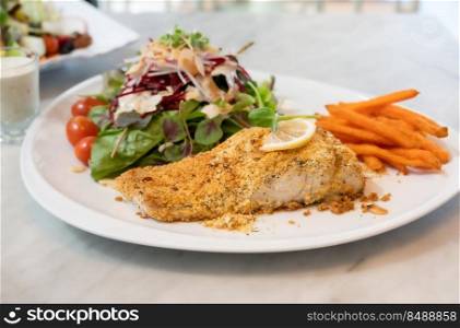 Grilled sea bass fish steak with herb crust and vegetables on a white plate
