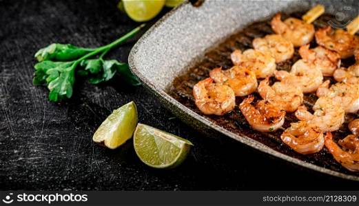 Grilled shrimp in a frying pan with parsley and pieces of lime. On a black background. High quality photo. Grilled shrimp in a frying pan with parsley and pieces of lime.