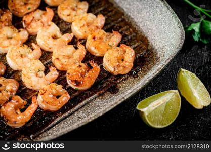 Grilled shrimp in a frying pan with parsley and pieces of lime. On a black background. High quality photo. Grilled shrimp in a frying pan with parsley and pieces of lime.