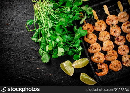 Grilled shrimp in a frying pan with parsley and pieces of lime. On a black background. High quality photo. Grilled shrimp in a frying pan with parsley and pieces of lime.