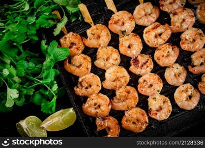 Grilled shrimp in a frying pan with parsley and pieces of lime. On a black background. High quality photo. Grilled shrimp in a frying pan with parsley and pieces of lime.