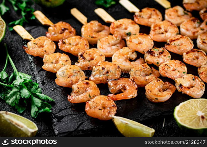 Grilled shrimp on a stone board with parsley and lime. On a black background. High quality photo. Grilled shrimp on a stone board with parsley and lime.