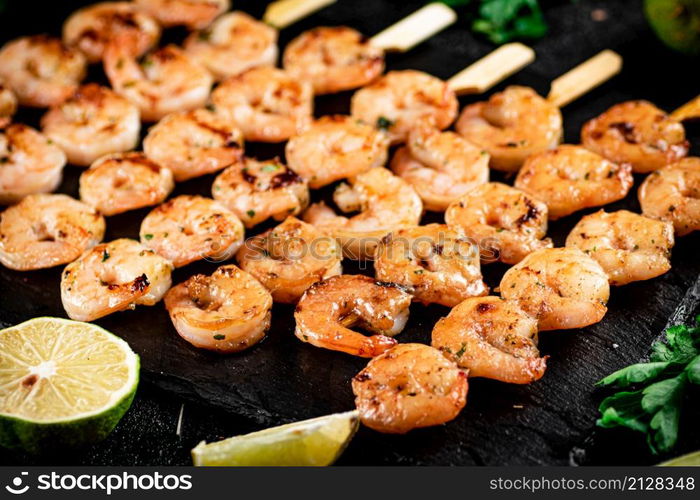 Grilled shrimp on a stone board with parsley and lime. On a black background. High quality photo. Grilled shrimp on a stone board with parsley and lime.