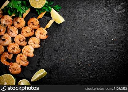 Grilled shrimp on a stone board with parsley and lime. On a black background. High quality photo. Grilled shrimp on a stone board with parsley and lime.