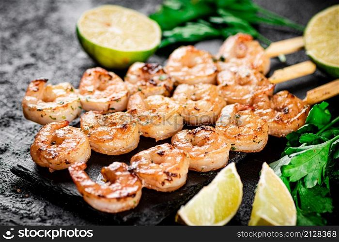 Grilled shrimp on a stone board with parsley and lime. On a black background. High quality photo. Grilled shrimp on a stone board with parsley and lime.